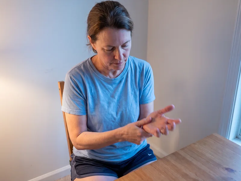 A woman sitting at a table rubbing her sore wrist and hand